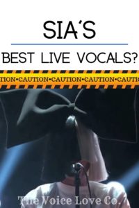 Singer, Sia, in a long wig that covers her face completely, sings into a mic. A giant black bow sits atop her two toned black and white wig. Text: Sia's Best Live Vocals? Proceed with CAUTION! A Voice Coach Reacts Video Presented by The Voice Love Co. 